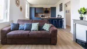 Una sala de estar moderna con un sofá marrón, una cocina al fondo y una chimenea.