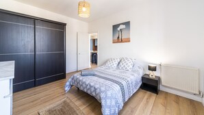 Un dormitorio con cama, mesita de noche, lámpara y un cuadro en la pared.