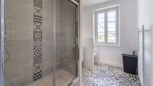 Un baño con ducha, azulejos decorativos, una ventana y un cubo de basura.