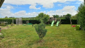 A grassy backyard with a wooden play structure, a small tree, and a green slide.
