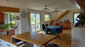 A spacious kitchen with a wooden table, a dining area with chairs, a staircase, and a large clock on the wall.