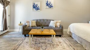 Une chambre avec un canapé gris, une table basse en bois, un tapis à motifs et deux œuvres d’art encadrées accrochées au mur.