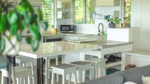 A modern kitchen with white cabinetry, a central island with stools, a microwave, and a sink. - Casa Aves - Gorgeous Ocean & Jungle View 3BR w/ Pool (nosara)