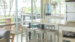 A kitchen with a large island, white bar stools, and a view through the glass door to the outside. - Casa Aves - Gorgeous Ocean & Jungle View 3BR w/ Pool (nosara)