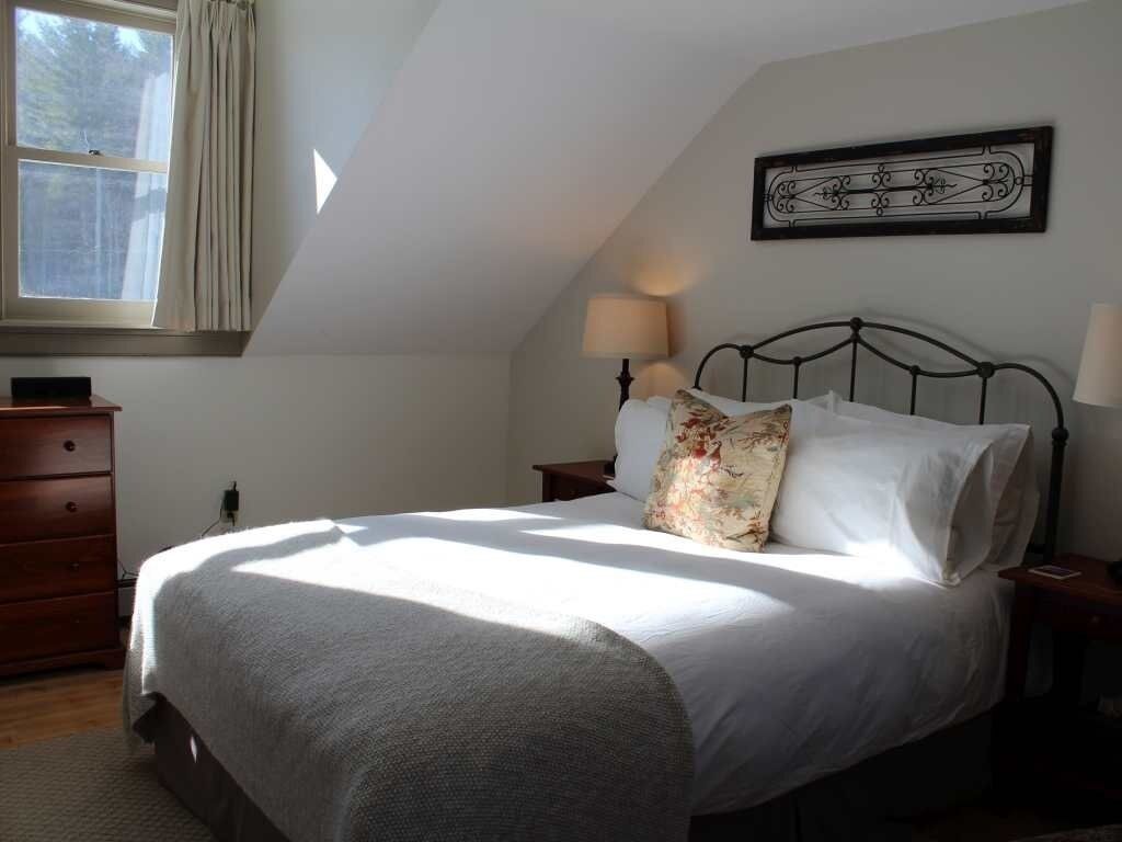 A bedroom with a bed, a nightstand, a dresser, a window, and a wall-mounted picture.