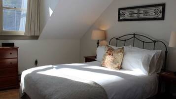 A bedroom with a bed, a nightstand, a dresser, a window, and a wall-mounted picture.