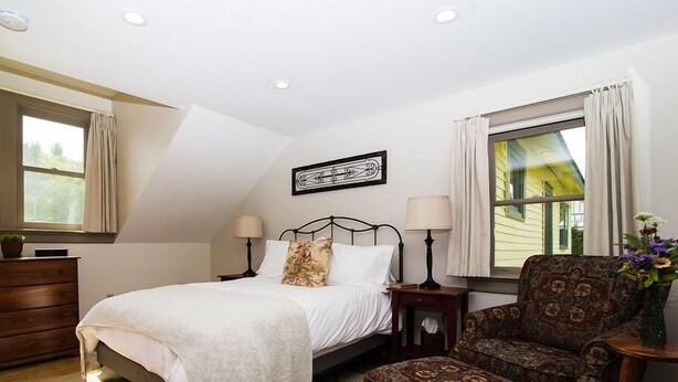 Une chambre à coucher comprenant un lit, deux tables de chevet, une chaise, une commode et une fenêtre avec des rideaux.