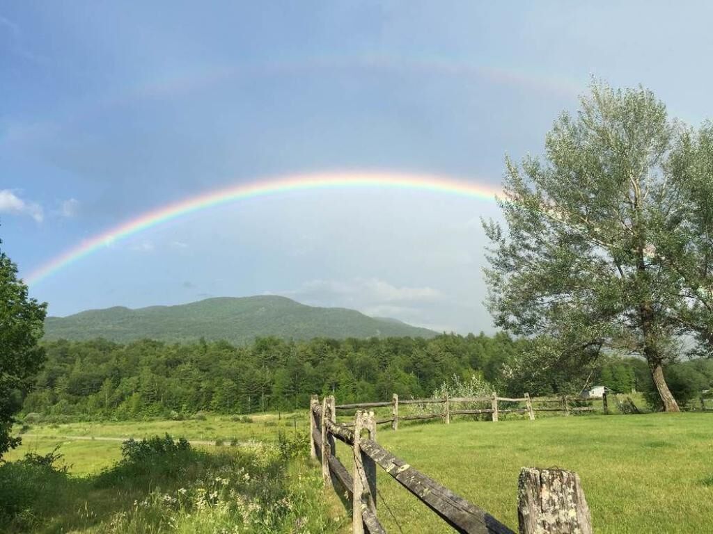 A rural landscape with a rainbow, a wooden fence, and a tree.