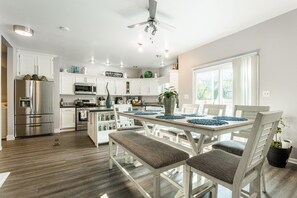 A modern kitchen with white cabinets, stainless steel appliances, and a dining area with a table set for four. - Cosmos Stays, Open Space, Jacuzzi, King Beds, Hot Tub, Serene, Spacious (Bolingbrook)