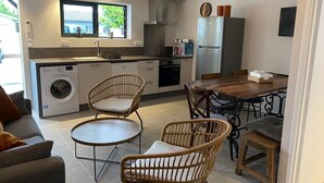 Una cocina compacta con lavadora, dos sillas de mimbre, una mesa de comedor y un refrigerador.