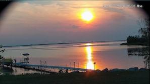 Un atardecer sobre una superficie de agua tranquila, con un muelle y sillas.