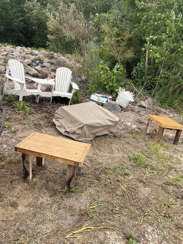 Un espace extérieur aménagé dans un style rustique, avec des chaises et des tables en bois, entouré de rochers et de verdure.