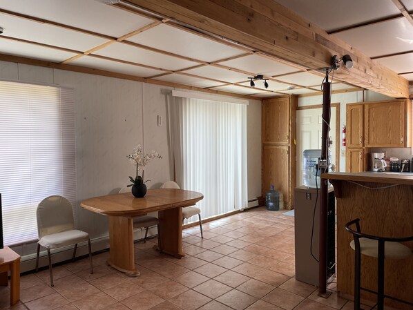 A dining area with a wooden table and chairs, a potted orchid, and a kitchen area with wooden cabinets and a water dispenser.