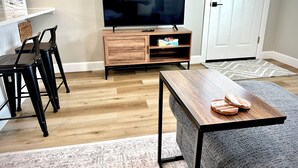 Una sala moderna con un mueble de televisión de madera, un televisor de pantalla plana, una mesa de comedor y dos taburetes de bar.