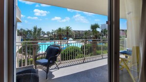A balcony with wicker chairs, a view of a swimming pool, and palm trees. - On the Brink of the Gulf, 3BR with a 3 Minute Walk to the Beach (Destin)
