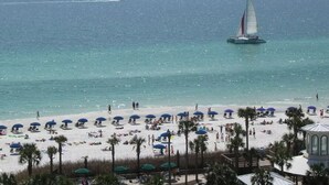 A beach with umbrellas and palm trees, a sailboat in the water, and a clear sky. - On the Brink of the Gulf, 3BR with a 3 Minute Walk to the Beach (Destin)