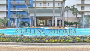 A hotel named Sterling Shores with a central pool, surrounded by palm trees and a flower bed. - On the Brink of the Gulf, 3BR with a 3 Minute Walk to the Beach (Destin)
