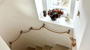 A spiral staircase with a rope handrail, a window with a striped blind, and a small shelf with decorative items.