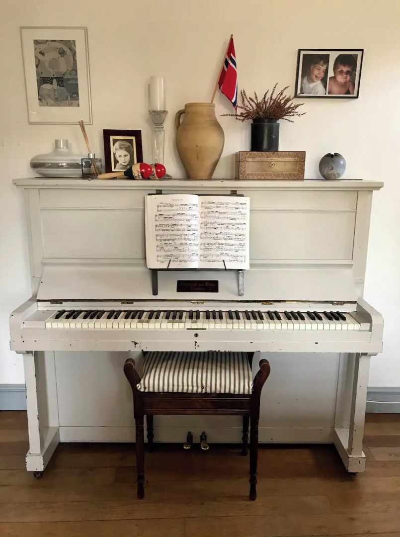 Een piano met bladmuziek, een stoel en diverse decoratieve objecten op een schoorsteenmantel.