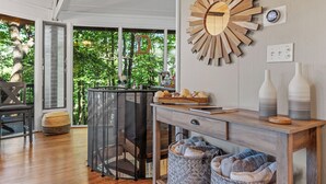 A modern living room with a wooden coffee table, a decorative sunburst wall clock, and a view of greenery through large windows. - Treetop Getaway with AMAZING lake views! (Jasper)