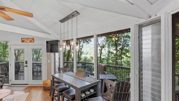 An outdoor deck with a wooden table and chairs, a television, and a view of the surrounding trees. - Treetop Getaway with AMAZING lake views! (Jasper)