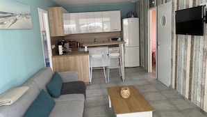 Um espaço de estar compacto com cozinha compacta, um sofá com almofadas, uma mesa de centro e uma TV na parede.
