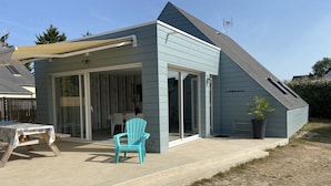 Uma casa com varanda coberta, porta de correr de vidro e um pequeno jardim com um vaso de planta.