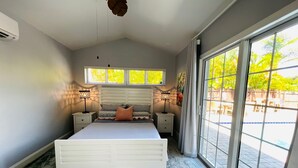 Een slaapkamer met een groot bed, twee nachtkastjes, een raam met gordijnen en uitzicht op een buitenruimte.