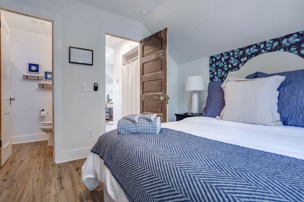 Una camera da letto con un letto grande, una porta in legno, un comodino con una lampada e una mensola a muro con un quadro incorniciato.