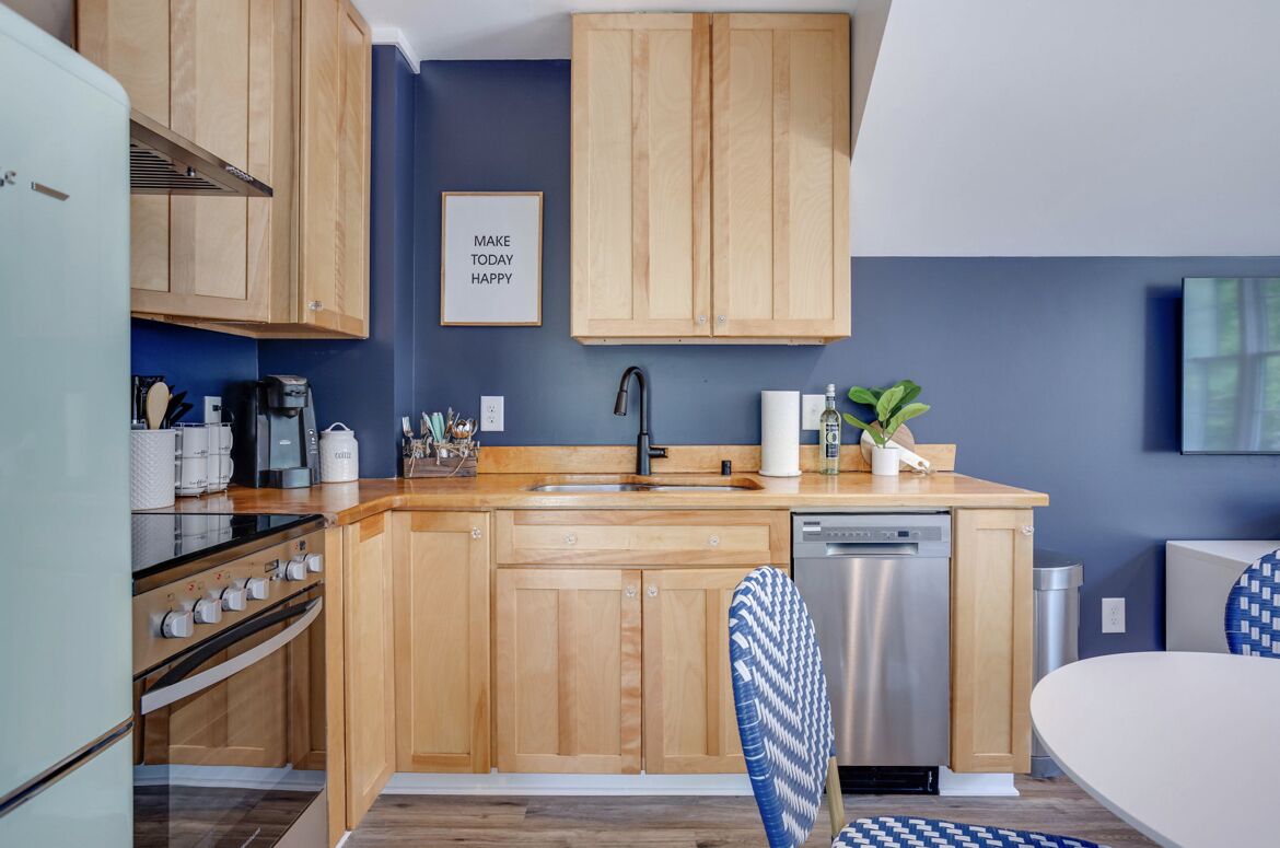 A compact kitchen with wooden cabinets, a stainless steel dishwasher, and a coffee machine.