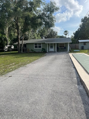 A residential house with a driveway leading to a front door, surrounded by trees and a grassy yard.