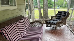 A covered porch with a wicker sofa and chairs, a tiled floor, and a view of a grassy yard. - Cute, clean home on big private lot in Inverness FL. (Inverness)