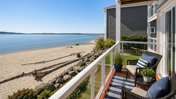 Un balcon donnant sur une plage, une chaise en osier, une plante en pot et un tapis à rayures.