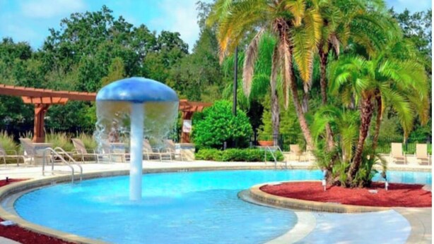 Una piscina con una fontana, circondata da palme e lettini.