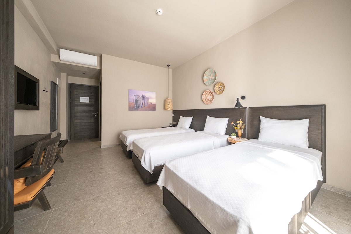 Quarto de hotel com duas camas, televisão, escrivaninha e uma cadeira.