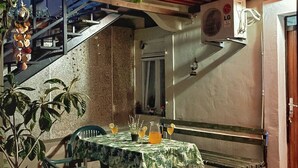 Een overdekte eethoek buiten met een tafel, stoelen en potplanten.