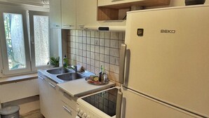 Een compacte keuken met witte kastjes, een inbouwoven, een spoelbak en een koelkast.
