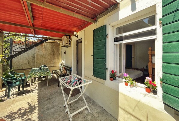 Une terrasse couverte avec une table, des chaises et un étendoir. Un escalier mène à un niveau supérieur.