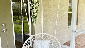 Una silla colgante de macramé blanco con un cojín, un adorno de pared de macramé blanco y una puerta con panel de vidrio.
