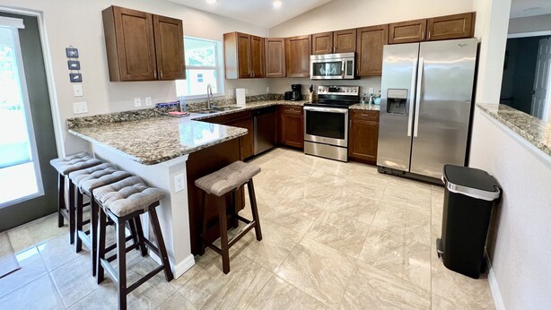 Una cocina moderna con encimeras de granito, electrodomésticos de acero inoxidable, armarios de madera y una isla central con taburetes de bar.