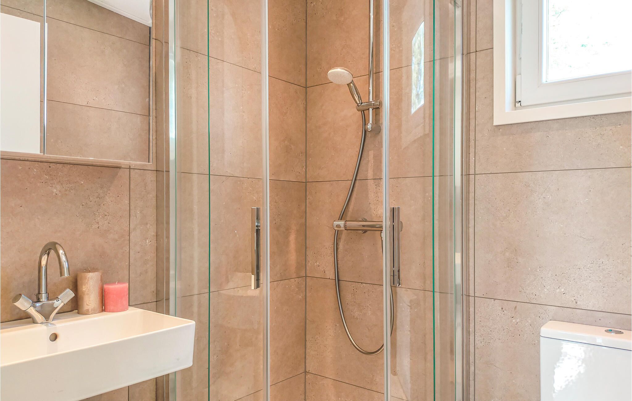 Een moderne badkamer met een douchecabine van glas, een witte wastafel en een toilet.