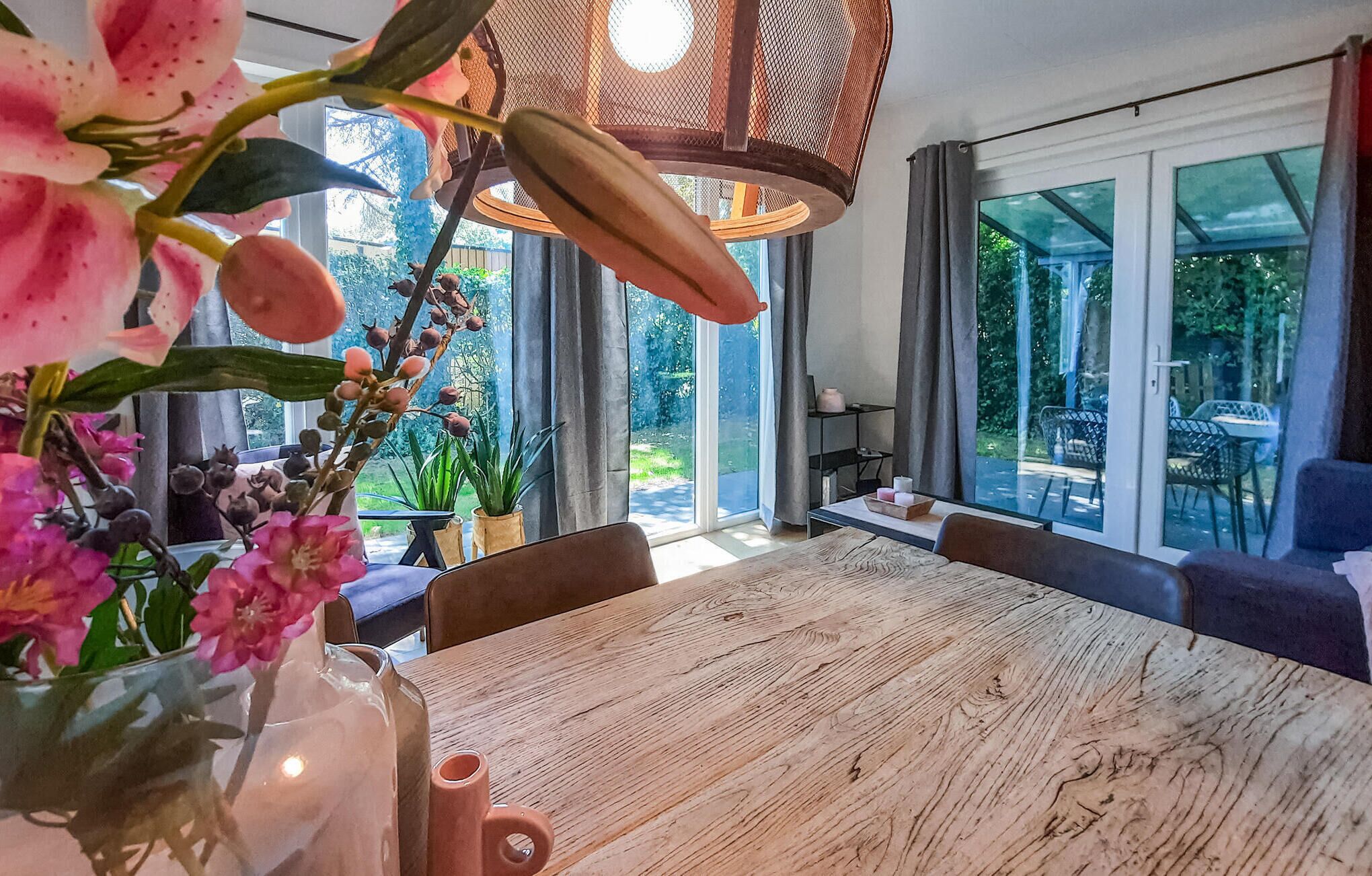 Un espace repas comprenant une table en bois, des chaises, un luminaire suspendu et une vue sur l’extérieur grâce à de grandes fenêtres.