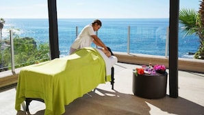 Een massagetafel met een groene hoes, een massagestoel en een klein tafeltje met bloemen.