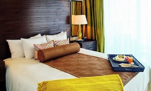 Camera d'albergo con un letto, cuscini, un comodino con una lampada, tende e un vassoio con prodotti per la colazione.
