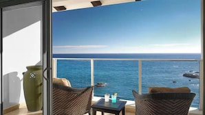 Een balkon met rieten stoelen, een tafeltje en uitzicht op de oceaan.