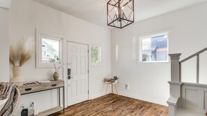 Una habitación amplia con piso de madera, paredes blancas, una puerta blanca, una mesita con una planta y una escalera con barandilla blanca.