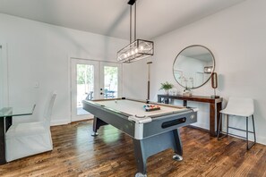 A modern living room with a pool table, a dining area with a glass table, and a wooden floor.