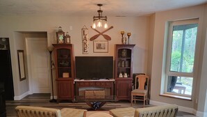 A living room with a fireplace, wooden furniture, a TV, and a large window. - Lake front LAWN FLOOR of bi-level home.
 bottom floor only. private entrance. (Dorena)