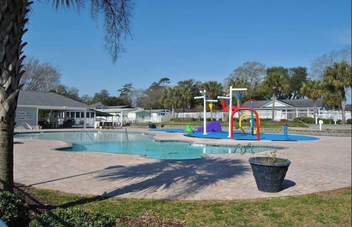 Une piscine avec un espace de jeux, entourée d’une terrasse dallée et de palmiers.