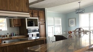 A kitchen with wooden cabinets, a central island, and a dining area with chairs and a table. - Coastal cottage minutes from the beach.  Large front porch for morning sun!! (Myrtle Beach)